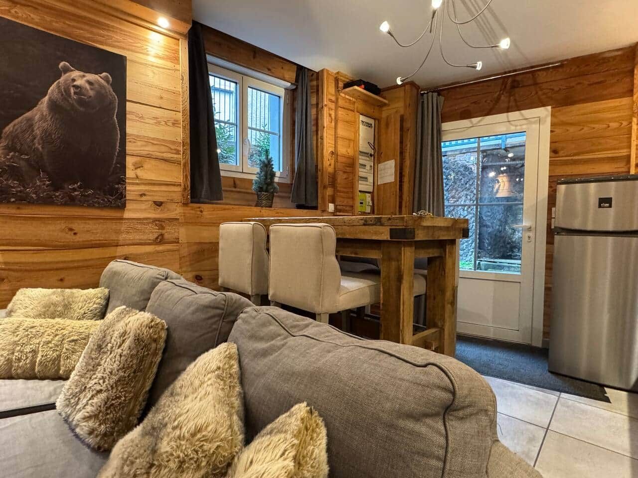 Interior acogedor de una cabaña con detalles de madera, un comedor con mesa y sillas, y un refrigerador.