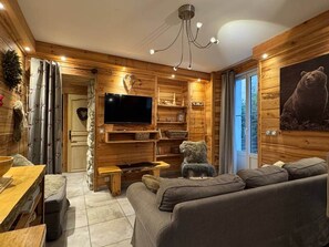 A cozy cabin interior with a wooden interior, a fireplace, a sofa, and a bear-themed wall decoration. - Le Tavae (Cauterets)