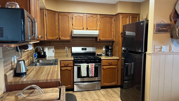 A kitchen with wooden cabinets, a stainless steel refrigerator, a stove, and a microwave. - Secluded cabin - 10 miles from Fredericksburg! (Fredericksburg)