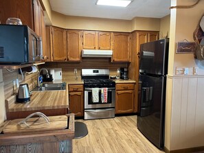 A kitchen with wooden cabinets, a stainless steel refrigerator, a stove, and a microwave. - Secluded cabin - 10 miles from Fredericksburg! (Fredericksburg)