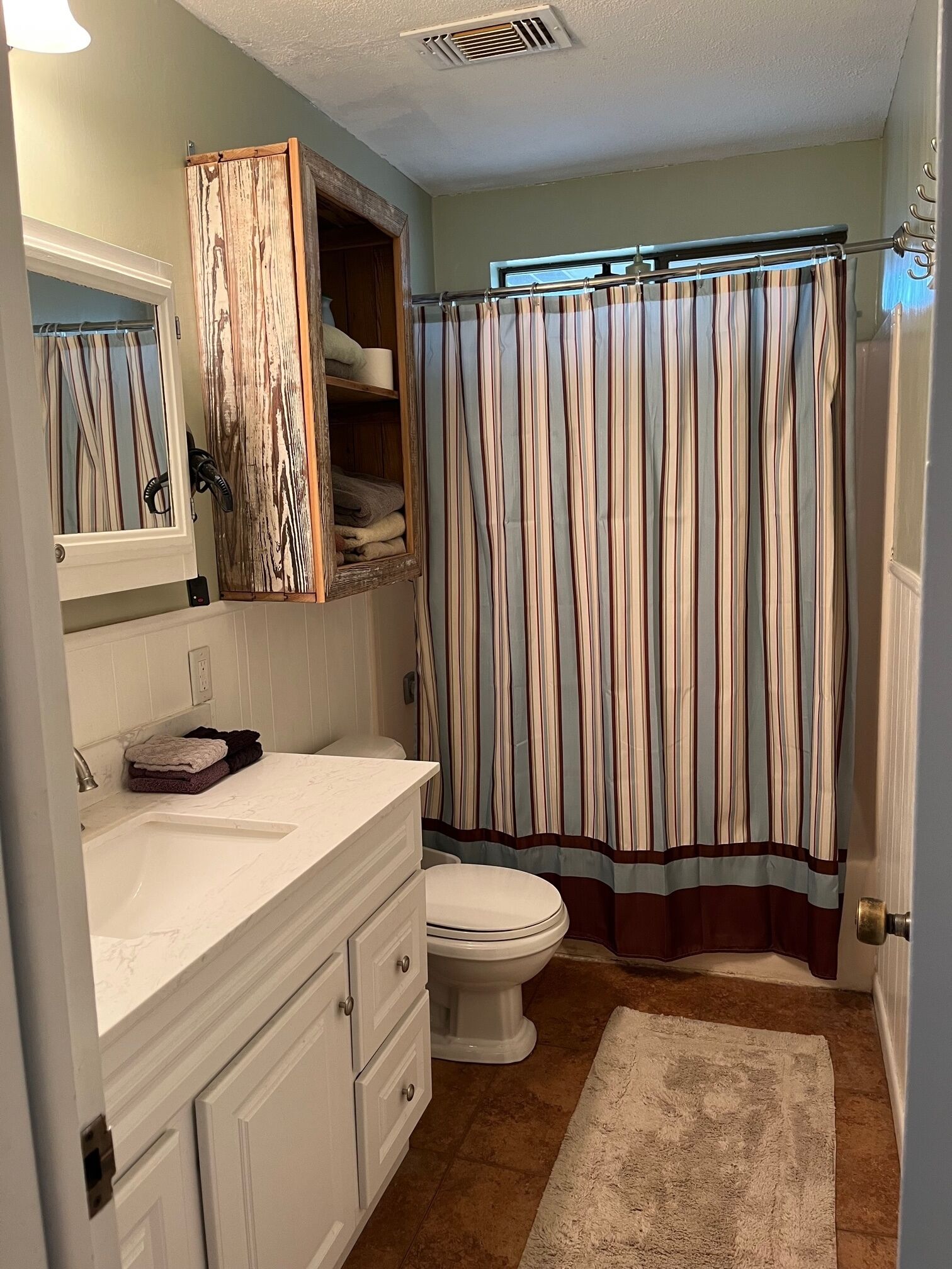 Une salle de bain avec un meuble-lavabo blanc, un placard en bois, un rideau de douche à rayures et des toilettes blanches.
