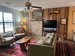 A living room with a fireplace, a television, and a ceiling fan. - Secluded cabin - 10 miles from Fredericksburg! (Fredericksburg)