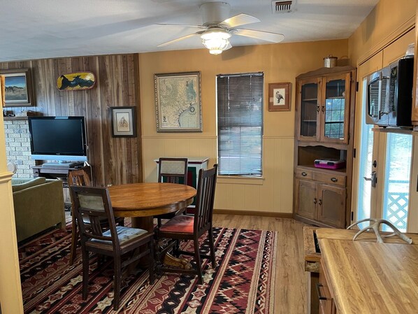 A dining area with a wooden table and chairs, a ceiling fan, and a television on a stand. - Secluded cabin - 10 miles from Fredericksburg! (Fredericksburg)