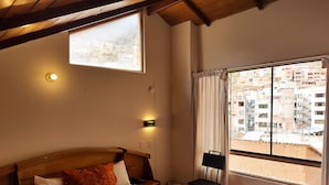 A hotel room with a bed, a window with curtains, a small table, and a chair. - Eco Bunnu Inn (Cusco)