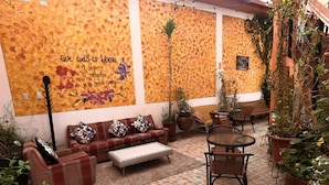 A cozy patio area with a sofa, chairs, and a small table. There are potted plants and a wall with a floral mural. - Eco Bunnu Inn (Cusco)