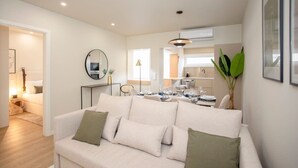 A modern living room with a sofa, a dining table, and a kitchen in the background.