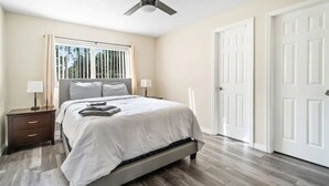 A bedroom with a bed, a nightstand, a ceiling fan, and a window with blinds.