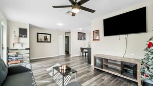A modern living room with a flat-screen TV, a ceiling fan, a coffee table, and a sofa.