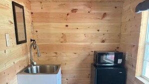 A compact kitchen with wooden walls, a sink, a microwave, and a small refrigerator.