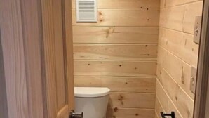 A small, wooden-paneled bathroom with a toilet and a trash can.