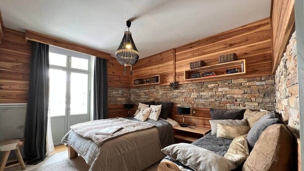 Ein Schlafzimmer mit einem großen Bett, einem kleineren Bett, einem Nachttisch, einer Kommode, einer Kristallleuchtreiter und einer Steinwand.