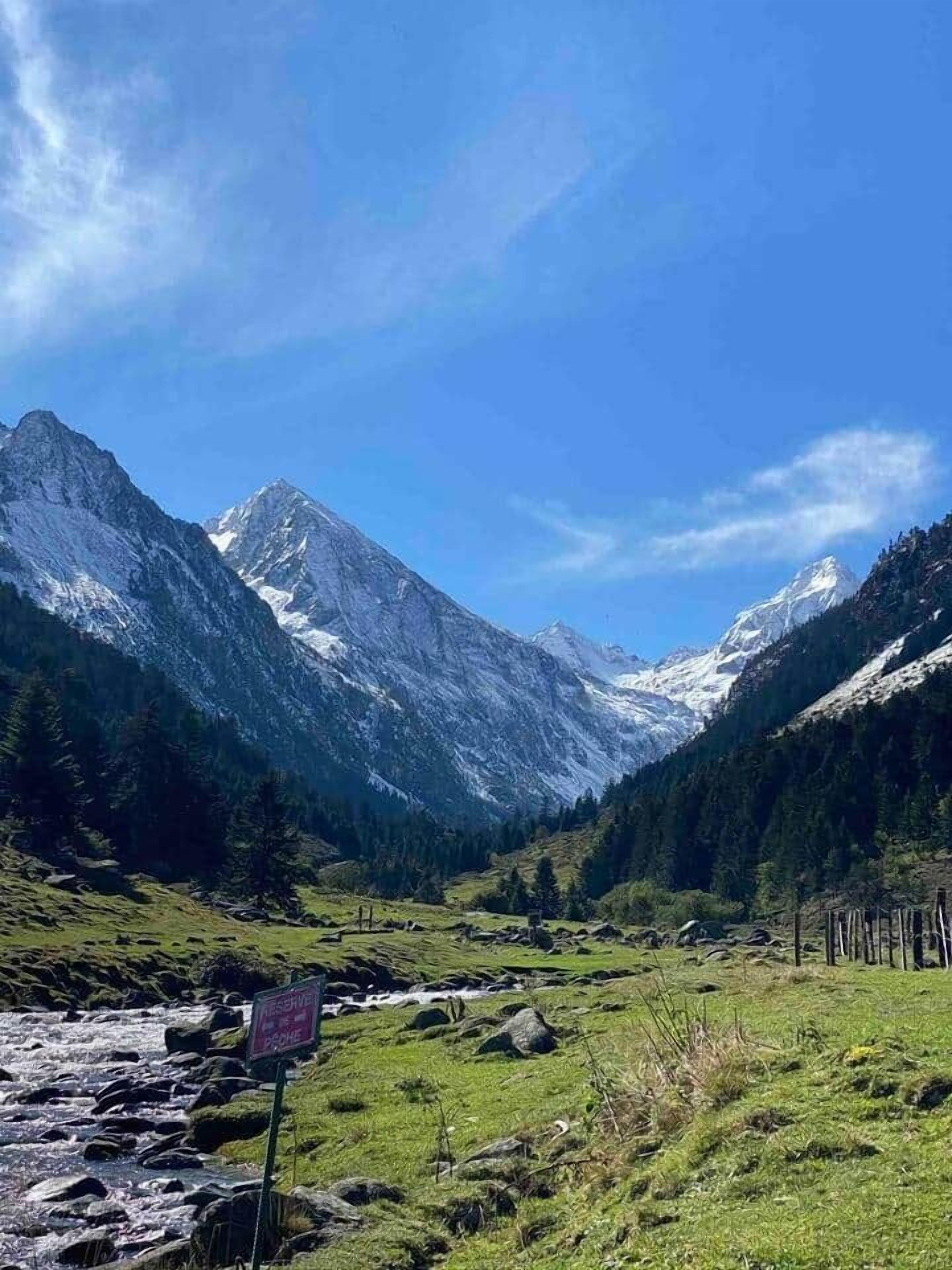 A mountain landscape with a clear sky, a river, and a sign indicating a reservation area.