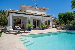 Une maison moderne dotée d’une piscine, d’un espace salon extérieur et de plantes en pot.