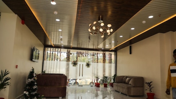 A spacious living area with a large window, a chandelier, and several pieces of furniture including a sofa and a chair. - Sarla Hotel Inn (Noida)