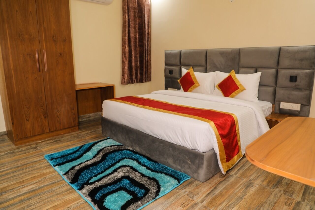A hotel room with a bed, a wooden wardrobe, a bedside table, a red and white bedspread, and a blue patterned rug.