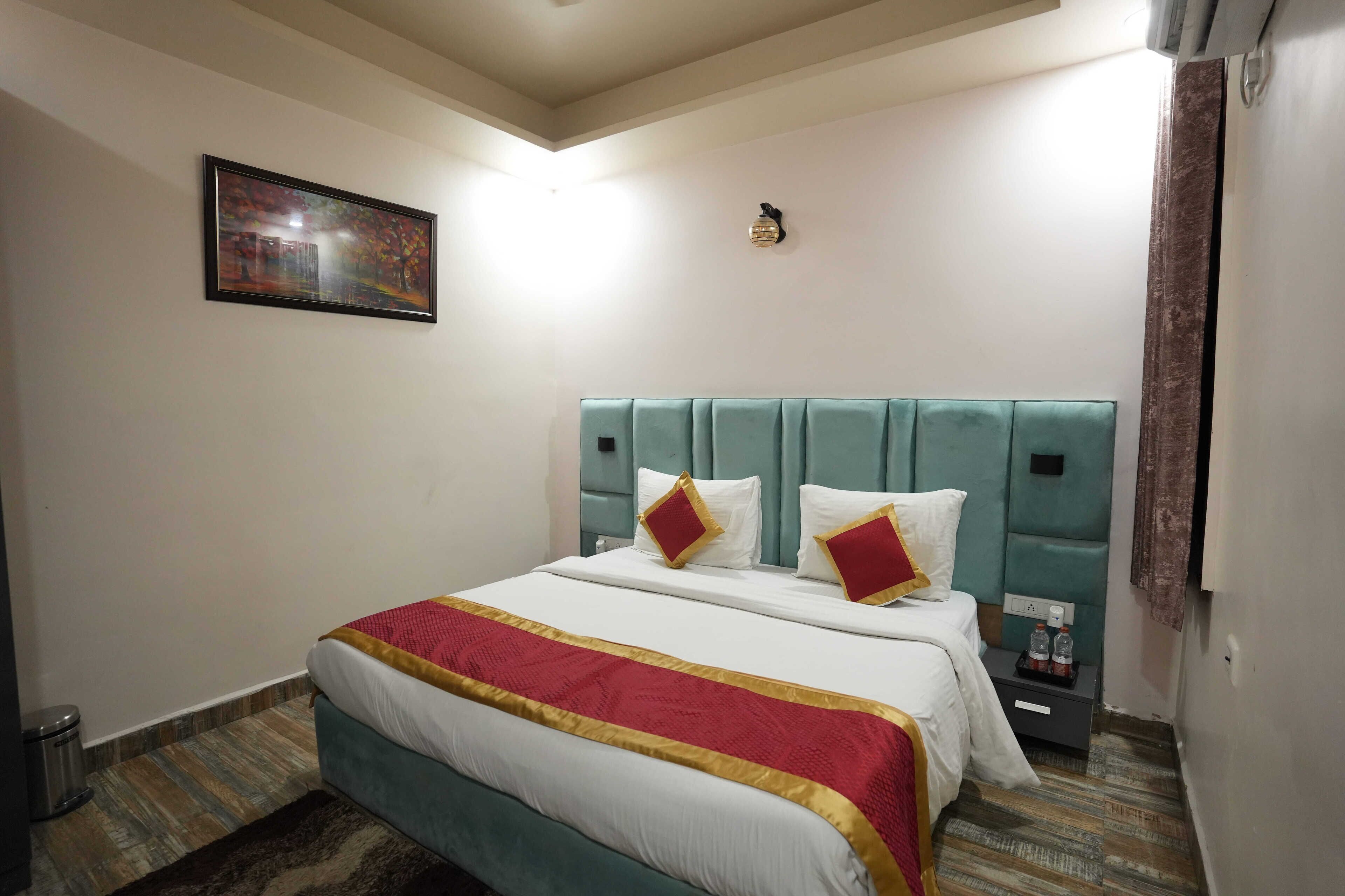 A hotel room with a bed, a nightstand, a wall-mounted light, and a framed picture.