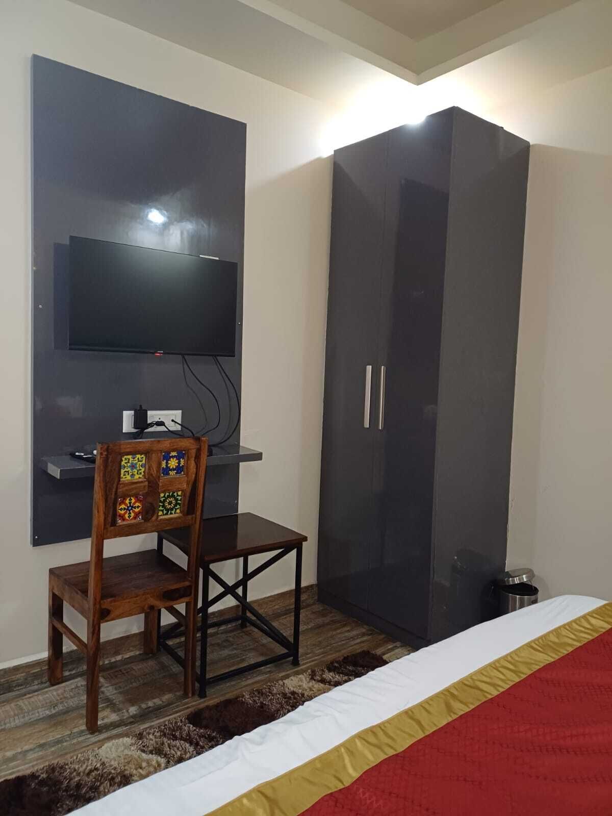 A room with a bed, a TV mounted on the wall, a wardrobe, and a small table with a chair.