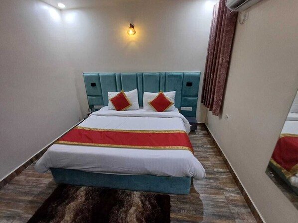 A hotel room with a bed, a headboard, a wall-mounted light, and a window with curtains.