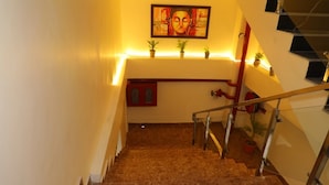 A staircase with a handrail, a red wall, and a Buddha painting above it. - Sarla Hotel Inn (Noida)