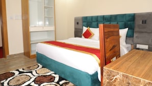 A bedroom with a bed, a wooden nightstand, a wardrobe, and a mirror. - Sarla Hotel Inn (Noida)