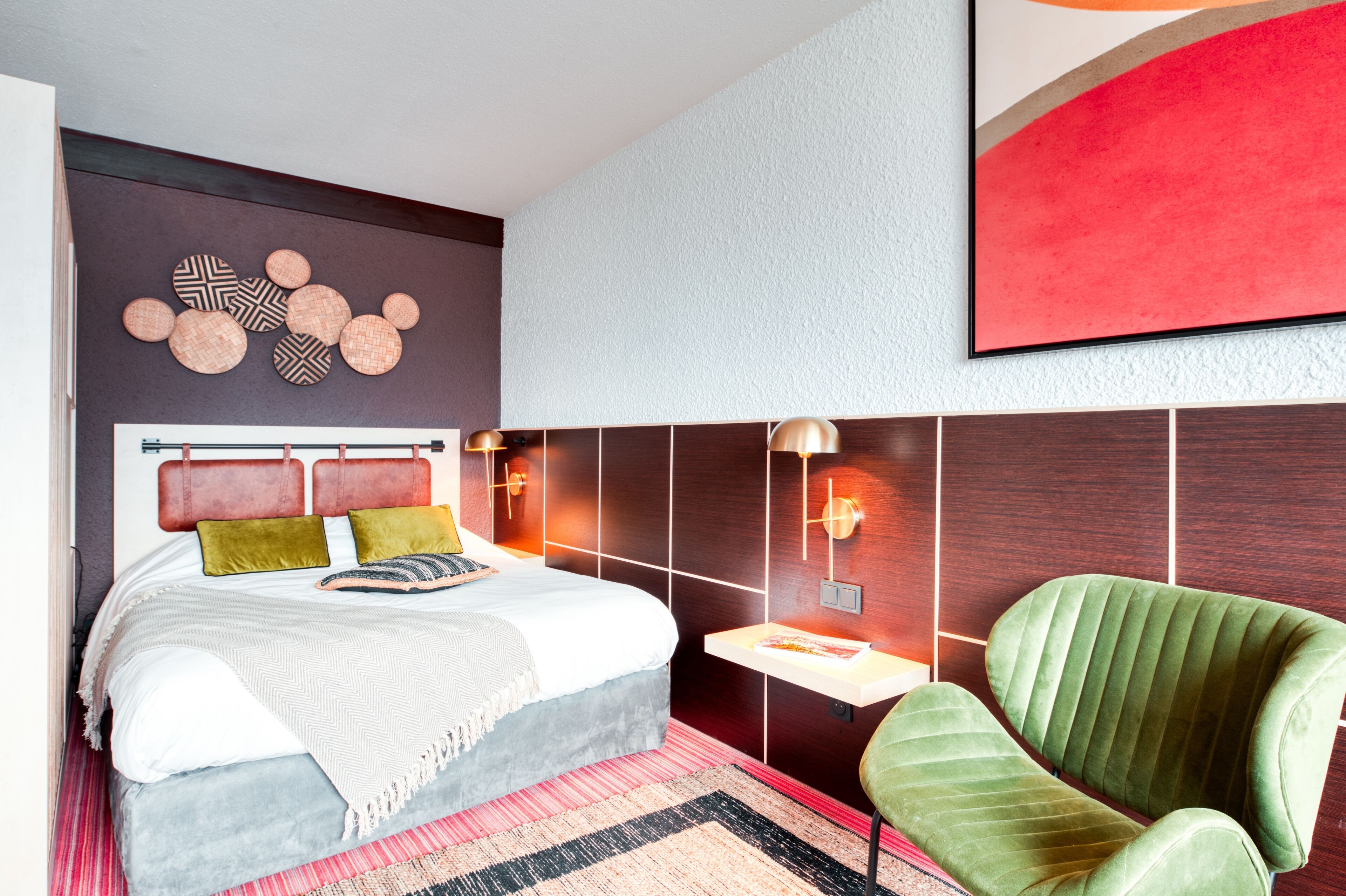 Ein modernes Schlafzimmer mit Bett, grünem Sessel und Wanddeko.