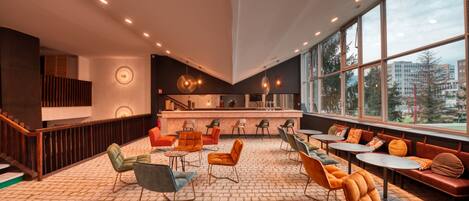 Un espacio interior amplio con diversas opciones de asientos, incluyendo sillas y sofás, una zona de bar y una escalera que sube a un nivel superior.