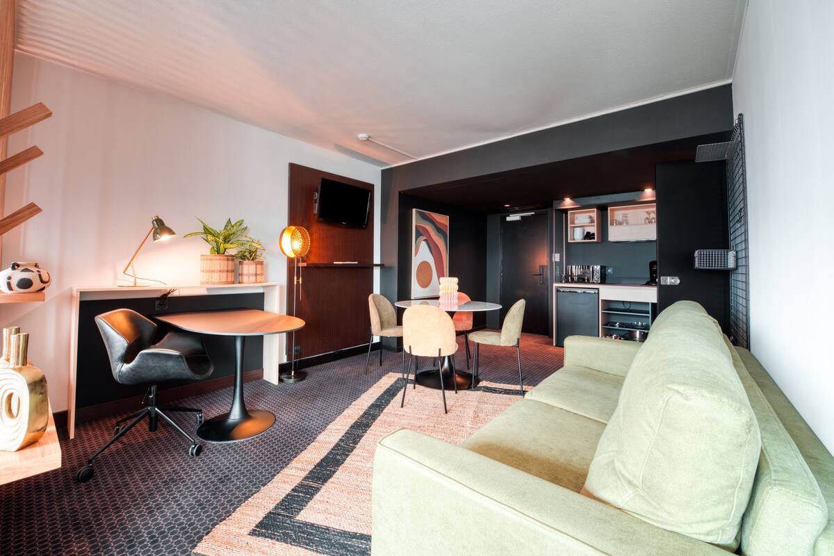 Una sala de estar moderna con un sofá, una mesa de comedor con sillas, una pequeña cocina y un televisor montado en la pared.