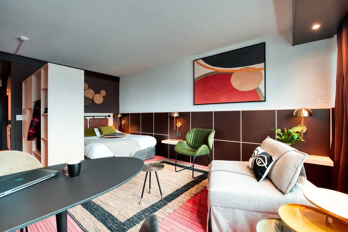 Una habitación de hotel moderna con una cama, un sofá, una mesa de comedor, una silla verde y una obra de arte colgada en la pared.