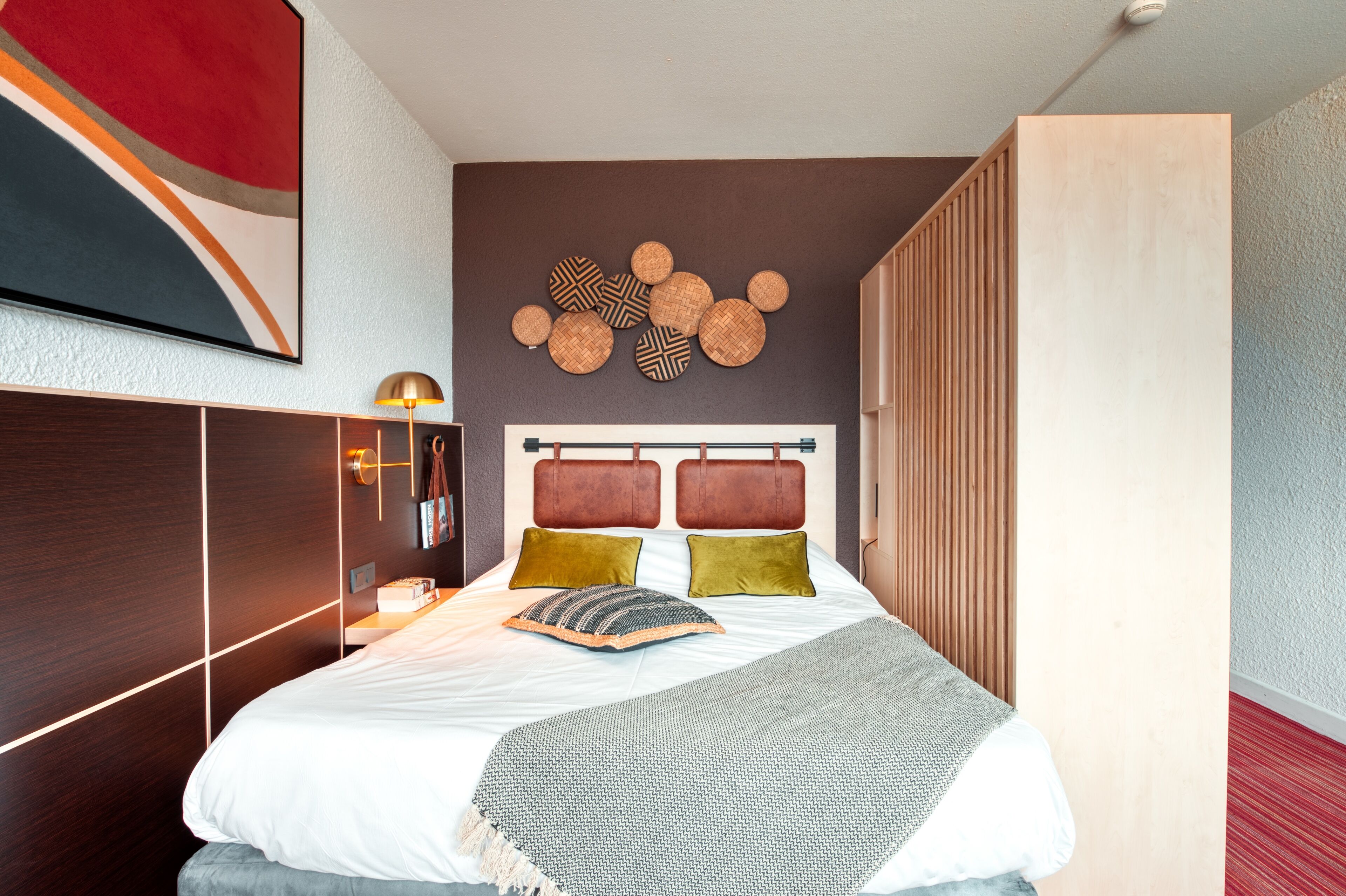 A modern hotel room with a large bed, a wooden wardrobe, a wall-mounted artwork, and a unique circular wall decoration.