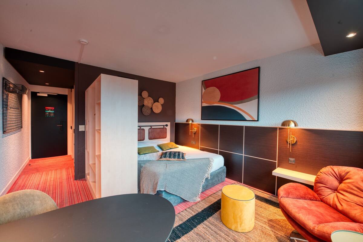 Una habitación de hotel moderna con una cama, un sofá, una mesita y un televisor montado en la pared.