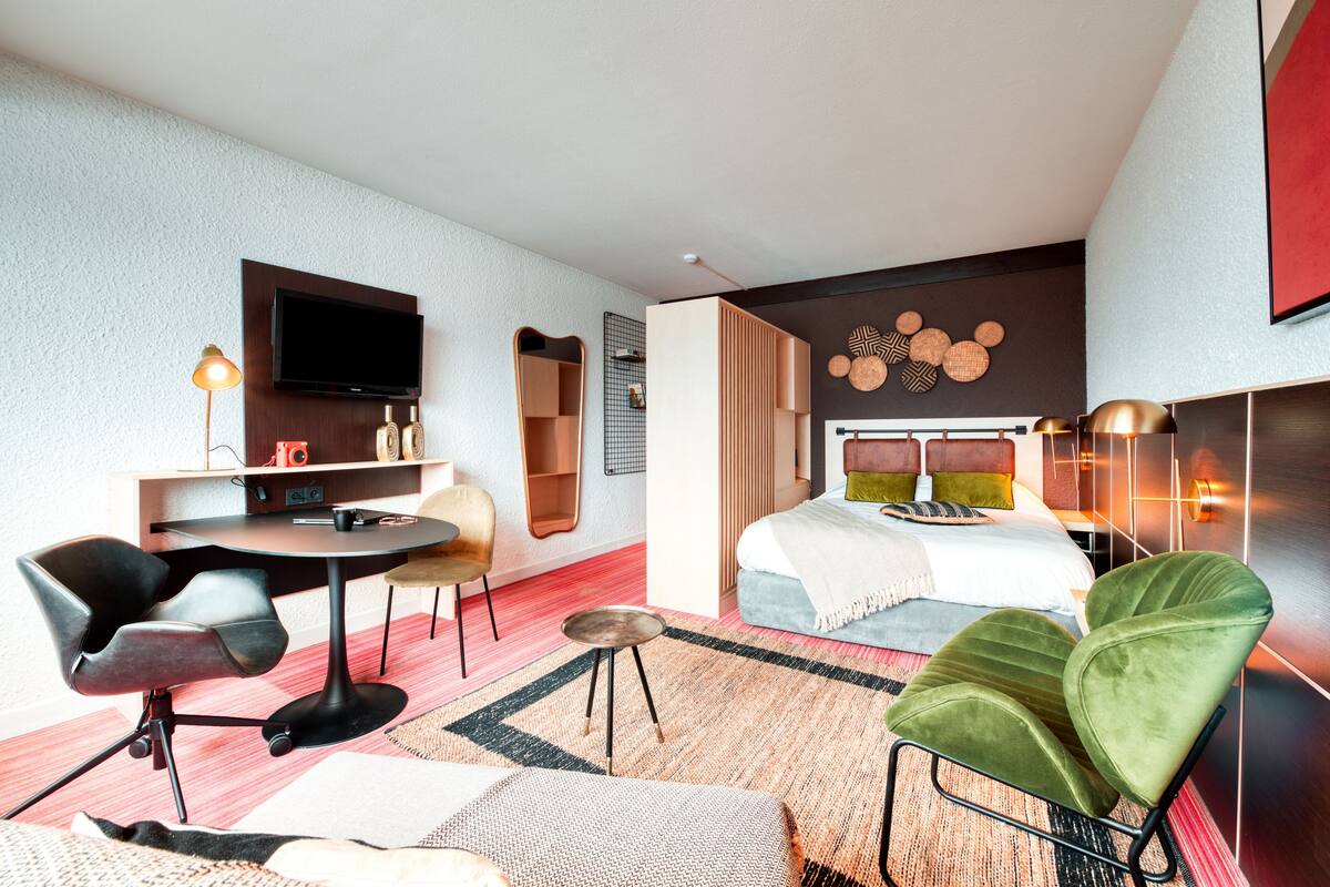 Una habitación de hotel moderna con cama, escritorio, televisión y zona de estar con sillas.