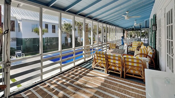 Un espacio de estar al aire libre cubierto con suelo a rayas, muebles de mimbre y grandes ventanales con vistas a una piscina y edificios.