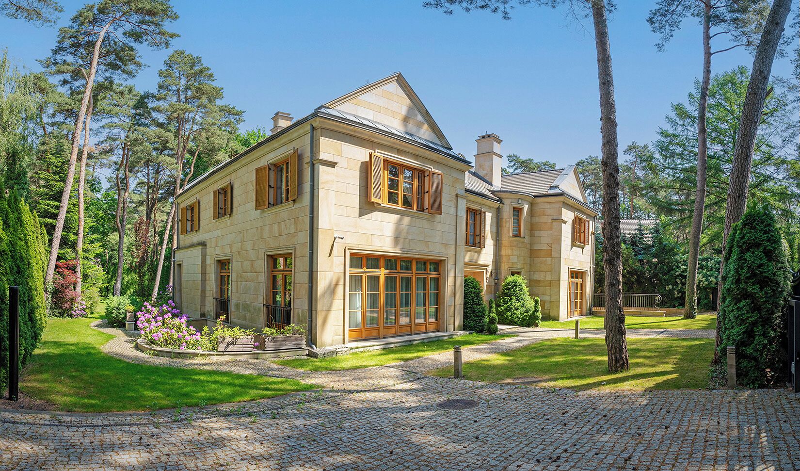 Ein zweistöckiges Steinhaus mit symmetrischer Fassade, großen Fenstern und einem gepflegten Garten mit Kopfsteinpflasterauffahrt.