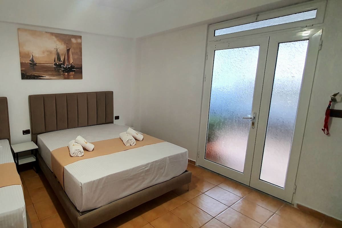 A hotel room with two beds, a painting of a seascape, and a sliding glass door to the outside.