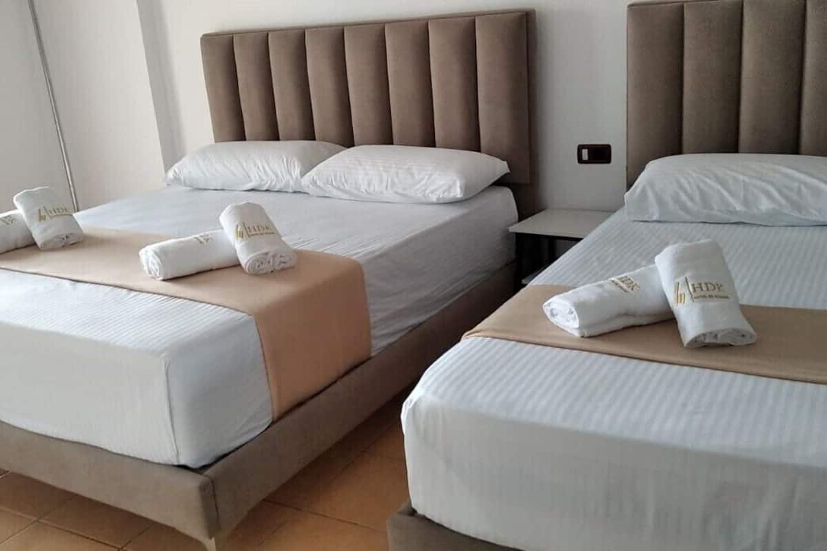A hotel room with two beds, each with a headboard, white linens, and rolled towels on the beds.