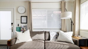 A modern living room with a sofa, a clock, a lamp, and a window with curtains. - Oasis Casita by Vacay in Tucson - Guesthouse on 4 peaceful desert acres (Tucson)
