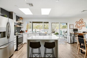 A modern kitchen with a central island, bar stools, and a view of the outdoors.
