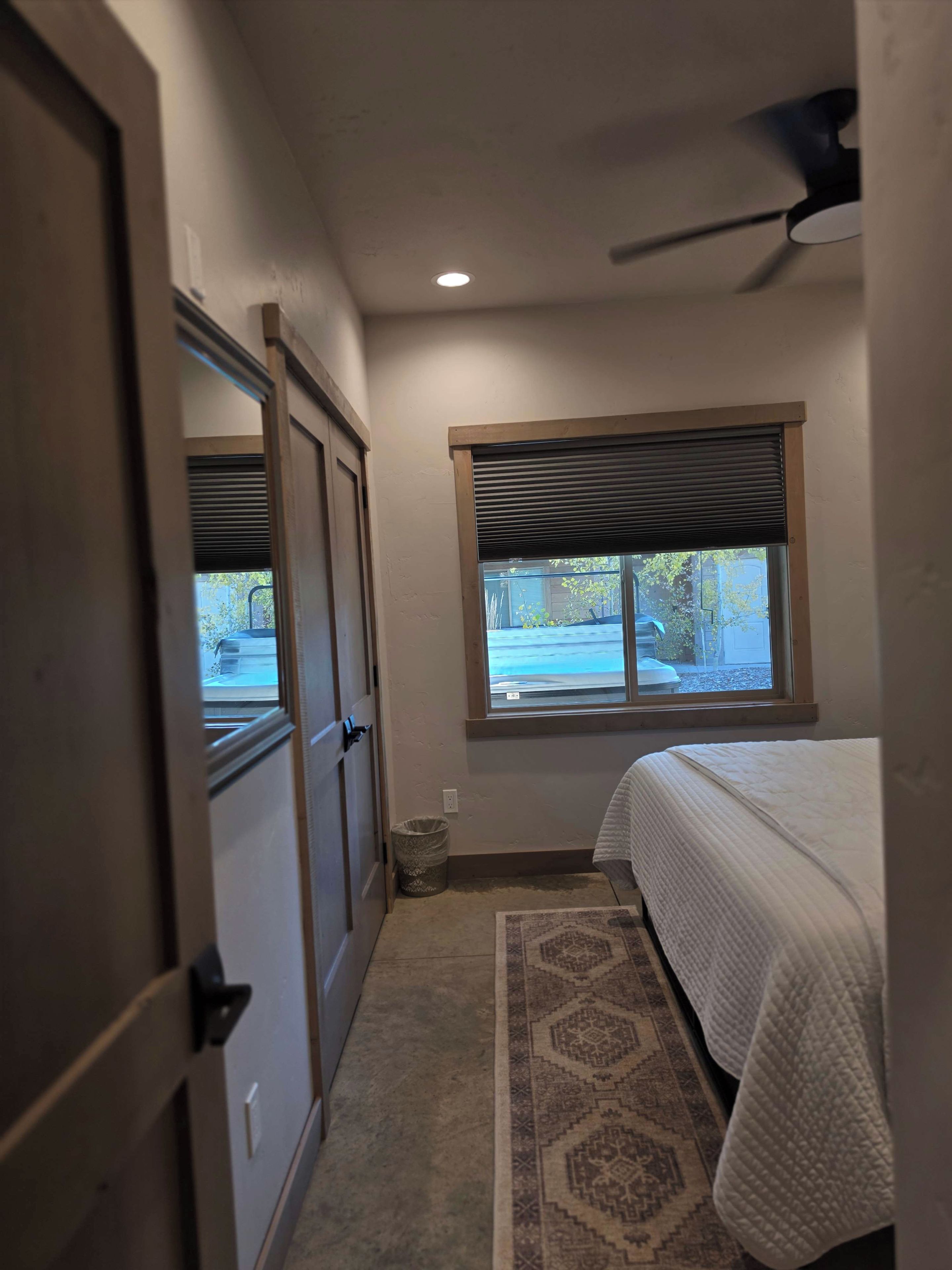 Un dormitorio con cama, ventana con persianas, ventilador de techo y piso alfombrado.