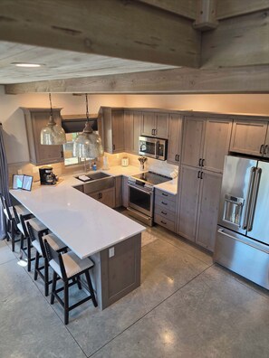 A modern kitchen with a large island, stainless steel appliances, and pendant lighting. - Coram Ridge Condo• 2BD/2BA• Hot Tub • 7 Mi to GNP (Coram)