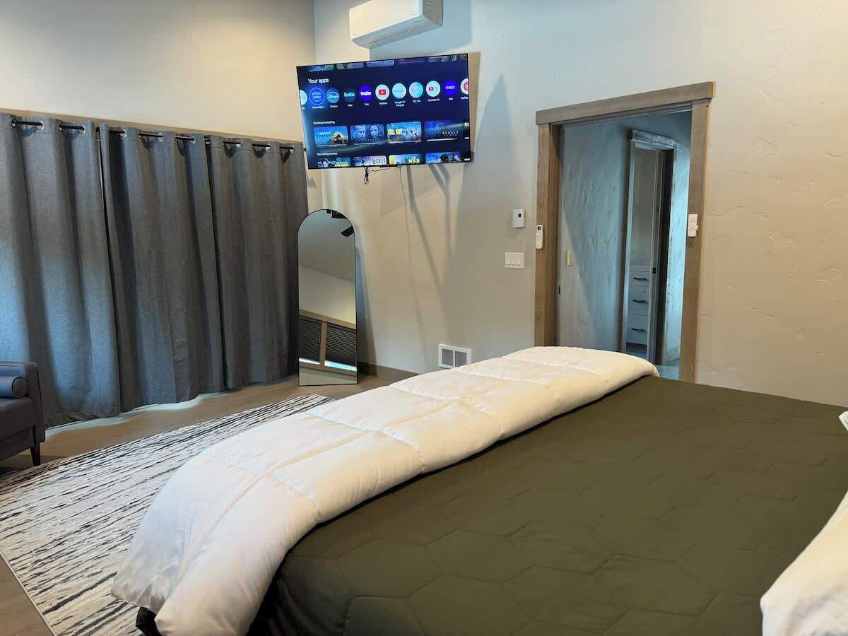 Een hotelkamer met een bed, een wandtelevisie, een spiegel en een deur.