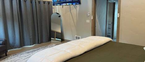 Een hotelkamer met een bed, een wandtelevisie, een spiegel en een deur.