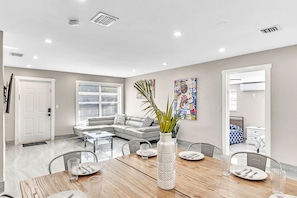 Relax in this stylish living space with a large sofa, dining table for four, and potted plant.