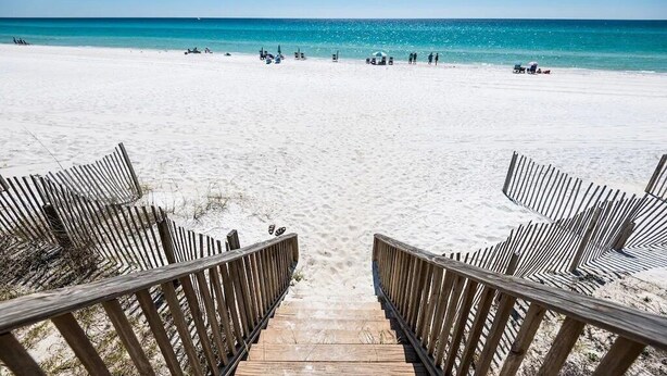 Une promenade en bois qui mène à une plage d’où l’on a une vue dégagée sur l’océan.