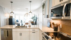 Une cuisine moderne avec des armoires blanches, des appareils en acier inoxydable et des luminaires suspendus.