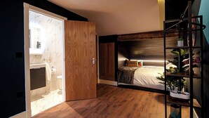 A bedroom with a wooden floor, a bed with a headboard, a bedside table, and a shelf with plants. - The Nest: Luxury 16 person Apt w jacuzzi & parking (Blackpool)