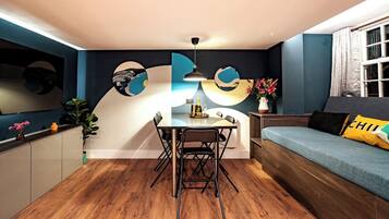 A modern living space with a dining area, a sofa with a cushion, a table with chairs, and a wall with abstract art.