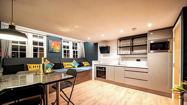 A modern kitchen with a dining area, wooden flooring, and a built-in oven. - The Nest: Luxury 16 person Apt w jacuzzi & parking (Blackpool)