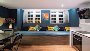 A modern living room with a blue sofa, a dining table with chairs, and a kitchen area with a stove. - The Nest: Luxury 16 person Apt w jacuzzi & parking (Blackpool)