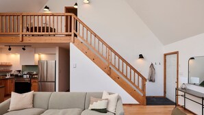 Un'ampia zona giorno con scala in legno, cucina dotata di elettrodomestici moderni e un angolo relax con divano e cuscini.
