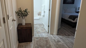 Un couloir mène à une salle de bain avec une douche, et la chambre adjacente contient un lit.